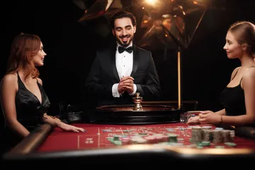 678DB Live Casino — Join thrilling real-dealer tables A professional dealer in a tuxedo greeting players at the roulette table, symbolizing the authentic live casino feel at 678DB.